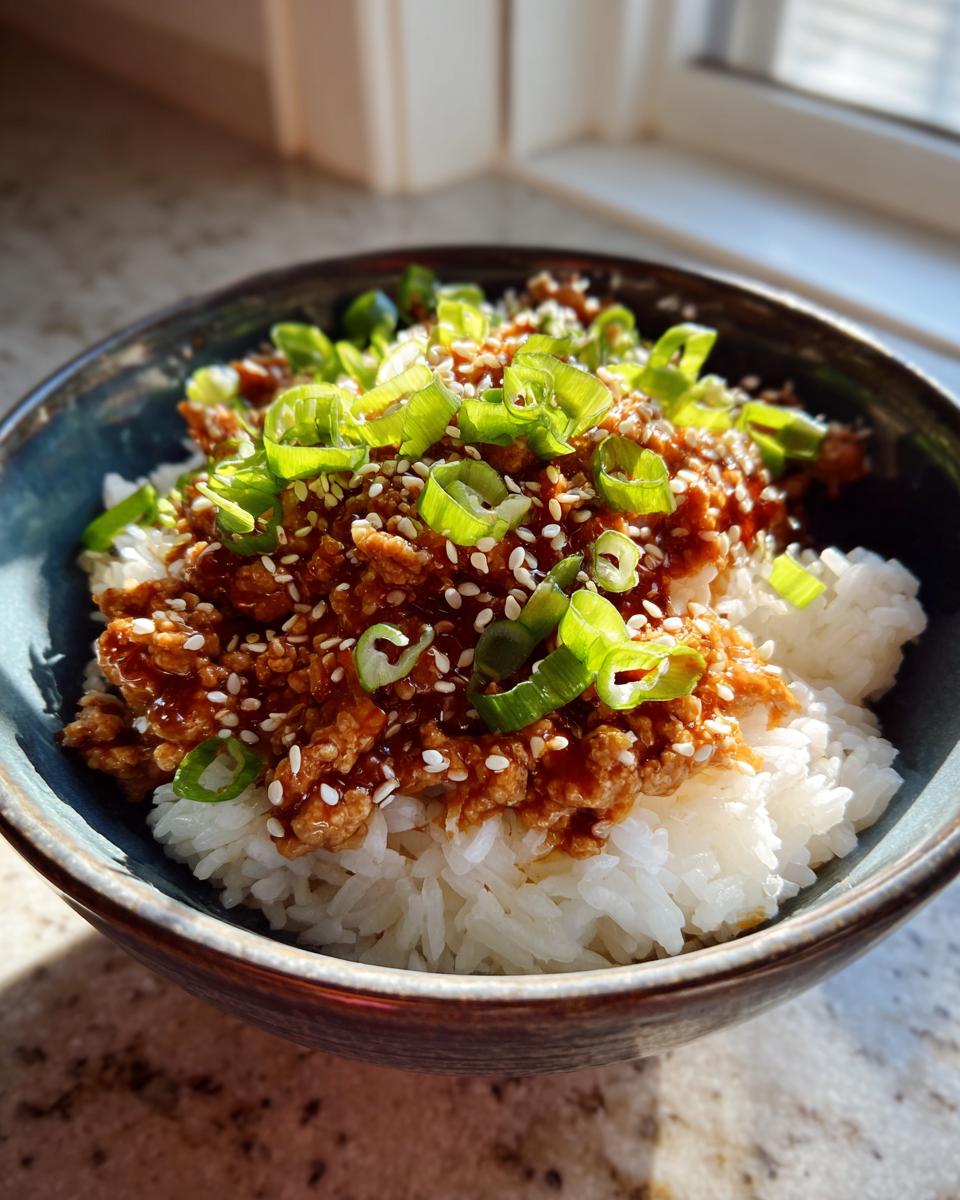 A close-up of a Teriyaki Turkey Rice Bowl featuring ground turkey in teriyaki sauce over white rice, topped with sesame seeds and sliced green onions.