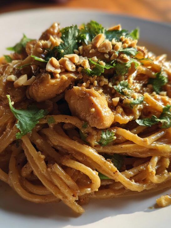 Close-up of a plate of creamy Thai Peanut Noodles With Chicken topped with cilantro and crushed peanuts.