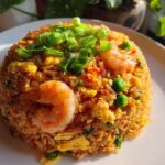 A mound of vibrant Thai Shrimp Fried Rice, featuring plump shrimp, green peas, scrambled egg, and topped with fresh green onions.