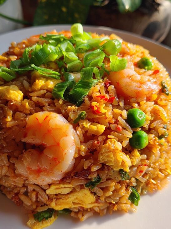 A mound of vibrant Thai Shrimp Fried Rice, featuring plump shrimp, green peas, scrambled egg, and topped with fresh green onions.
