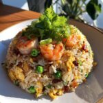 A perfectly mounded plate of Thai Shrimp Fried Rice topped with succulent shrimp, peas, egg, and fresh cilantro.
