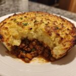 A close-up of a single serving of Vegan Lentil Shepherd Pie with a rich lentil filling and a golden, browned mashed potato topping.