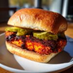 Close-up of a Vegan Nashville Hot Chicken Sandwich featuring a heavily spiced patty and pickle slices on a brioche bun.