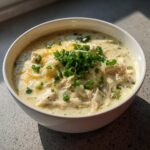 A close-up of a bowl of creamy White Chicken Enchilada Soup topped with shredded cheese and fresh green onions.