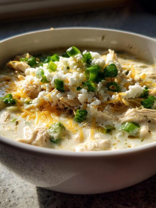 A close-up of a bowl of White Chicken Enchilada Soup topped with shredded chicken, cotija cheese, and green onions.