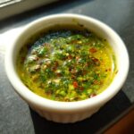 Close-up of vibrant green herbs, chili flakes, and oil in a white ramekin, showcasing the 5 Minute Zesty Chili Lime Marinade.