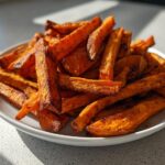 A close-up of a white plate piled high with perfectly seasoned Air Fryer Crispy Sweet Potato Fries, showing their orange color and crispy edges.