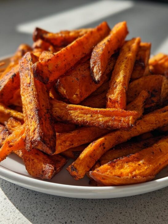 A close-up of a white plate piled high with perfectly seasoned Air Fryer Crispy Sweet Potato Fries, showing their orange color and crispy edges.