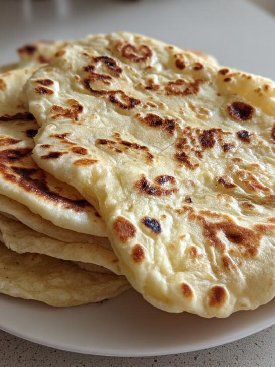 A stack of freshly cooked, soft flatbreads showing golden-brown blistered spots, representing The Only Bread Which You Can Eat As Much As You Like.