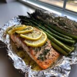 A perfectly cooked fillet of Baked Salmon In Foil With Asparagus topped with lemon slices and herbs.