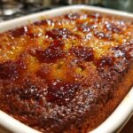Close-up of a golden brown Baked Sticky Rhubarb Pudding with a glistening, caramelized rhubarb topping in a white dish.