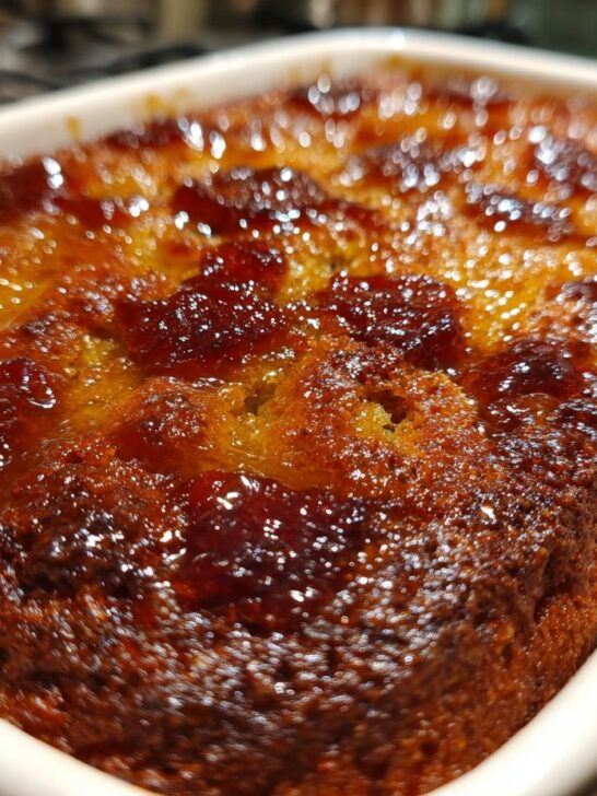 Close-up of a golden brown Baked Sticky Rhubarb Pudding with a glistening, caramelized rhubarb topping in a white dish.