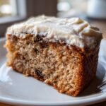 Close-up of a moist slice of Banana Bread Cake With Cream Cheese Frosting on a white plate.