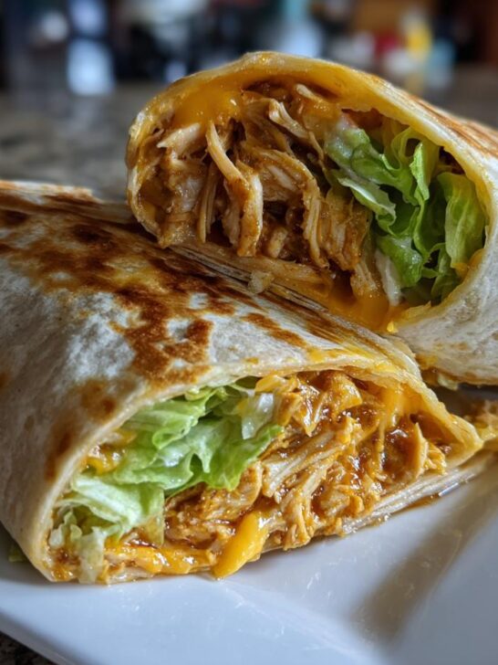 A close-up of a grilled Bbq Ranch Chicken Wrap cut in half, showing shredded chicken, melted cheese, and crisp lettuce.