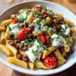 A close-up of Caprese Pasta With Italian Sausage featuring penne, ground meat, roasted tomatoes, fresh mozzarella dollops, and basil.