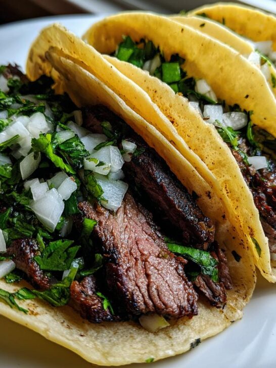 Close-up of three authentic Carne Asada Tacos filled with grilled steak, white onion, and cilantro on soft corn tortillas.