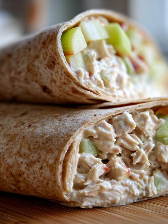 Close-up of two Chicken Apple Salad Wraps stacked on a wooden board, showing creamy filling and apple chunks.