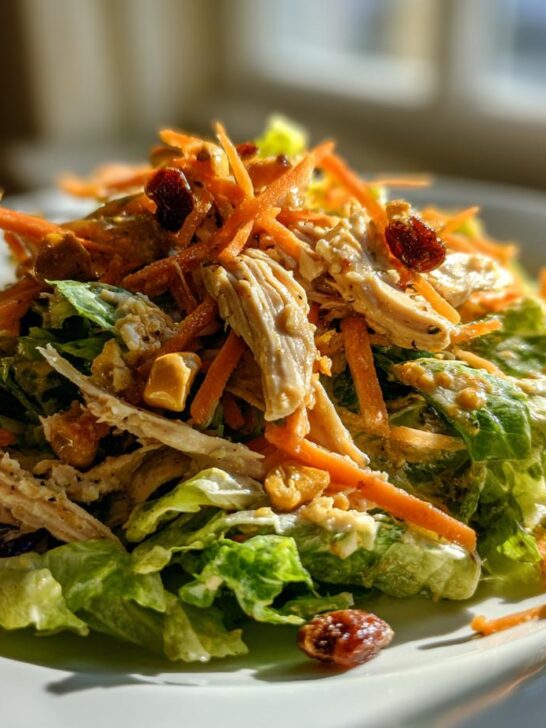 A vibrant mound of Chicken Cashew Crunch Salad featuring shredded chicken, carrots, cashews, and dried cranberries on lettuce.