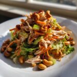A vibrant mound of Chicken Cashew Crunch Salad featuring shredded chicken, carrots, celery, and whole cashews on a white plate.