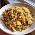 A close-up, top-down view of a bowl filled with flavorful Chinese Chicken Fried Rice, featuring rice, scrambled egg pieces, and green onions.