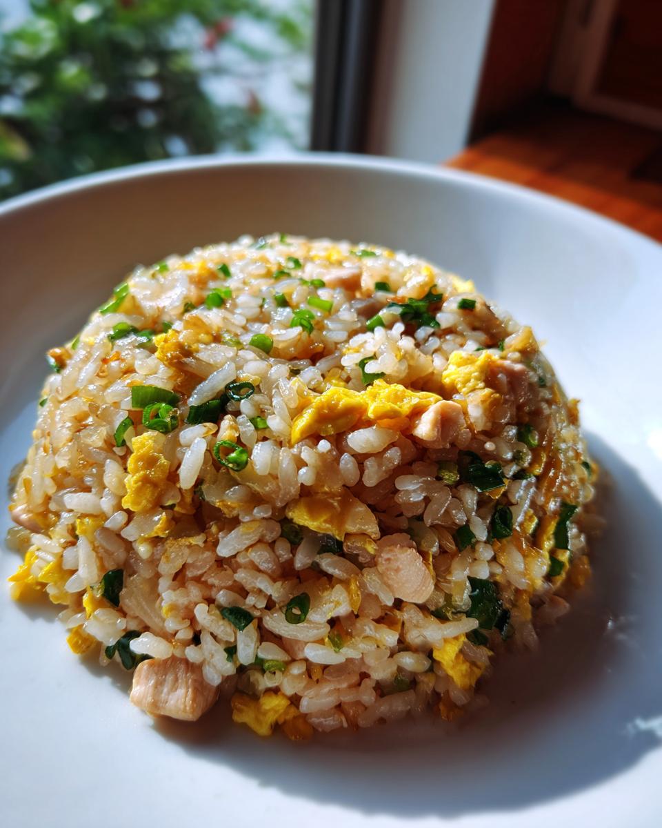 A mound of freshly made Chinese Chicken Fried Rice with visible pieces of egg, chicken, and green onions on a white plate.