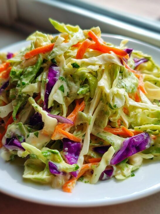 A close-up of vibrant Cilantro Lime Coleslaw featuring shredded green cabbage, purple cabbage, and carrots tossed in a creamy dressing.