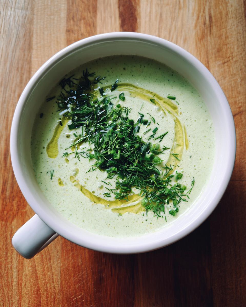 Overhead view of a bowl of Cold Cucumber Soup With Yogurt And Dill, topped with fresh dill, chives, and olive oil.