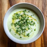Overhead view of Cold Cucumber Soup With Yogurt And Dill, garnished with fresh dill, parsley, olive oil, and pepper.