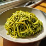 A bowl filled with spaghetti coated in bright green, creamy avocado pasta sauce, beautifully lit by sunlight.