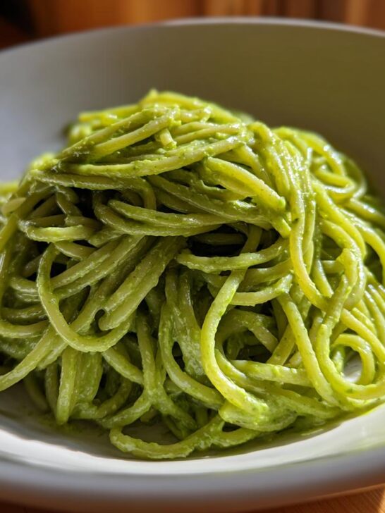 Close-up of spaghetti coated in bright green, creamy avocado pasta sauce served in a light bowl.