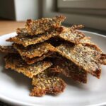 A close-up pile of golden brown, crispy Chia Flax Seed Crackers loaded with visible chia and sesame seeds.