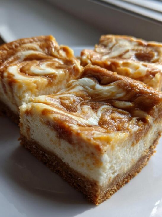Three thick, square Dulce De Leche Cheesecake Bars with a graham cracker crust, sitting on a white plate.