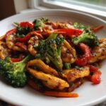 A close-up of a vibrant Potsticker Stir Fry featuring golden potstickers, bright green broccoli, and red bell peppers coated in a glossy sauce.