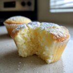 Close-up of a Fluffy Japanese Cotton Cheesecake Cupcake with a bite taken out, showing its airy texture and dusted with powdered sugar.