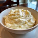 A close-up of fluffy Mashed Cauliflower With Sour Cream, topped with cracked black pepper, served in a white bowl.