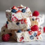 Close-up of stacked squares of Frozen Yogurt Bark With Berries, featuring visible strawberries and blueberries.