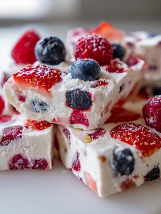 Close-up of stacked squares of Frozen Yogurt Bark With Berries, featuring visible strawberries, blueberries, and raspberries.