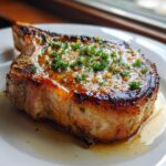 A perfectly cooked, thick-cut pork chop glistening with garlic butter sauce and topped with fresh parsley.