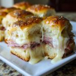 Close-up of a Glazed Ham And Cheese Sliders cut in half showing melted cheese pull.