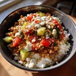 Close-up of a Greek Ground Turkey Rice Bowl topped with crumbled feta cheese, diced tomatoes, and cucumber.