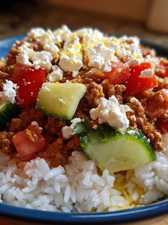 A close-up of a Greek Ground Turkey Rice Bowl featuring seasoned ground turkey over white rice, topped with diced tomatoes, cucumbers, and feta cheese.