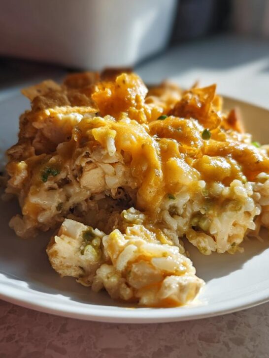 A serving of cheesy Green Chile Chicken And Rice Casserole with visible chicken, rice, and a crunchy topping on a white plate.