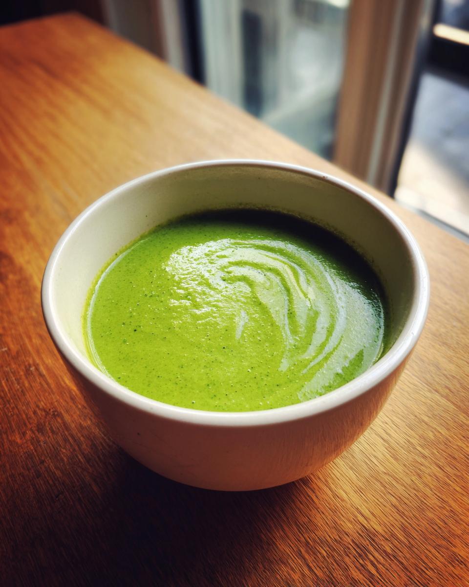 A close-up of vibrant Green Goddess Soup Recipe, perfectly blended and served in a white bowl on a wooden surface.