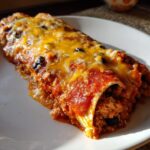 A close-up of two baked Ground Turkey Black Bean Enchiladas covered in red sauce and melted cheddar cheese.