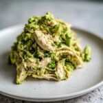 A mound of Healthy Avocado Chicken Salad featuring shredded chicken mixed with chunky avocado on a light speckled plate.