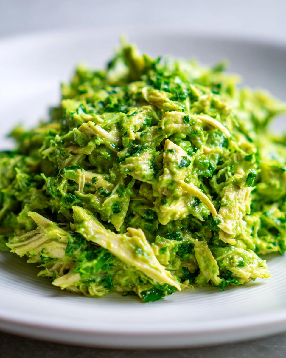 Close-up of shredded chicken mixed with creamy green avocado dressing in a Healthy Avocado Chicken Salad.