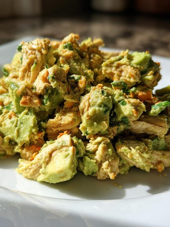A close-up serving of Healthy Avocado Chicken Salad featuring chunks of chicken mixed with bright green avocado chunks on a white square plate.