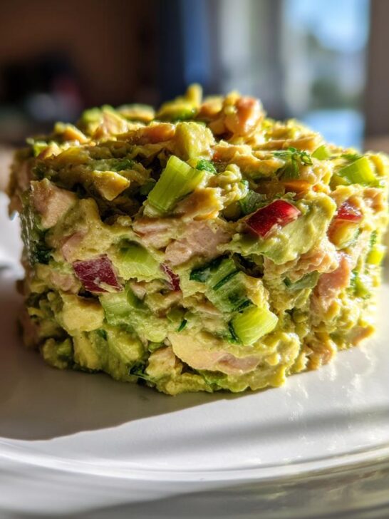 A molded serving of Healthy Avocado Tuna Salad featuring chunks of tuna, avocado, celery, and red onion on a white plate.