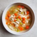 Overhead view of a bowl of shredded chicken soup with bright orange carrots and green celery, perfect for high protein low carb soups.