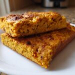 Two thick, golden-orange squares of High Protein Red Lentil Flatbread stacked on a white plate.
